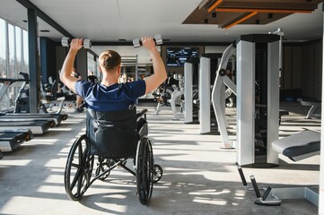 Obraz premium Man in wheelchair lifting dumbbells during rehabilitation in gym