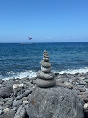 Stone cairn with parasailing in the background on sunny day.