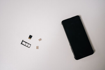 Sim cards and memory card positioned near sleek smartphone on white surface, representing mobile...