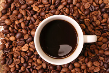 Fresh roasted aromatic arabica coffee bean smoking steaming white ceramic cup black drink on rustic jute fabric mat