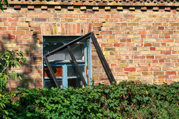 Broken window in an old brick house. The grate hangs on the broken window