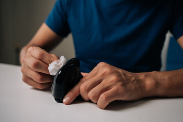 Close-up cropped shot of man cleaning modern black vertical mouse with disinfectant wipe, promoting hygiene and preventing spread of germs, sitting at white table in workplace or home office.