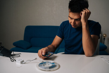 Puzzled electrician troubleshooting RGB led strip light setup, holding remote control and...