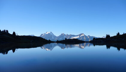 A tranquil morning reflection of snow-capped mountains and blue sky on a glassy lake