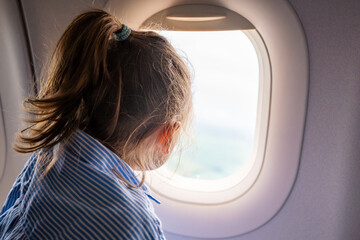 Little girl looking out the airplane window during a flight. Wonder, travel experience, and...