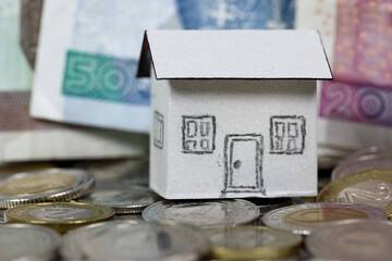 Coins and paper money, as well as a model of a gable-roofed, detached house made of paper