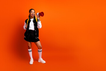 Energetic young woman holding a megaphone wearing a varsity jacket and smiling while standing...