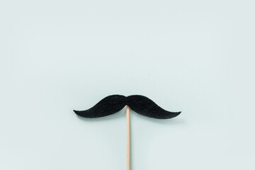 Black moustache on wooden stick on blue background. Creative concept for Father Day. Moustache month and challenge. Mens Health.