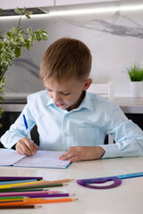 Boy does his homework on table at home. The development of child, his growth and preparation for a...