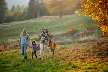 A portrait of young family with two small children in autumn nature at sunset.