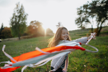 Girl playing with a rainbow hand kite in autumn nature at sunset.