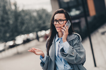 Confident young woman talking on phone outdoors in urban setting on a bright day wearing stylish and trendy coat