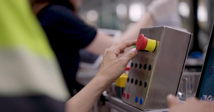 female engineer pressing emergency stop button during automation training session to test robot safety function while operating robotic arm on manufacturing control panel in smart industry40 lab