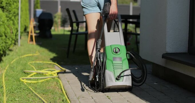 Woman pulling a high-pressure washer in the backyard of a house.