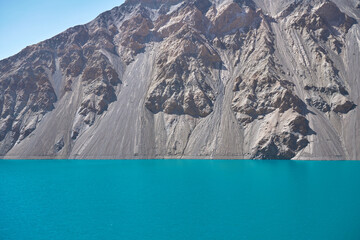 Stunning turquoise waters of a mountain lake against a backdrop of rocky slopes under a clear blue sky