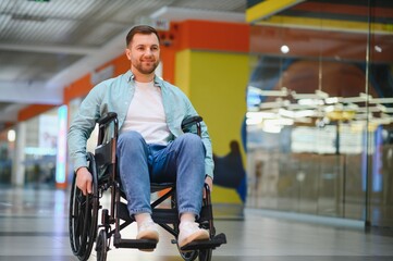Smiling man using wheelchair moving through shopping mall corridor