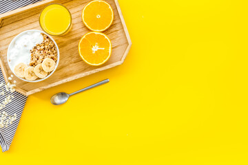 granola with banana slices and orange juice for breakfast on yellow background top view copyspace