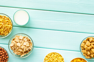 Various corn cereals in bowls and milk on mint wooden background top view copyspace