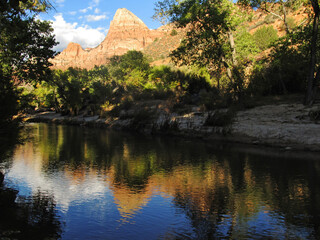 The Watchman towering over the Virgin River, reflecting the majestic peak, in the Zion Canyon in...