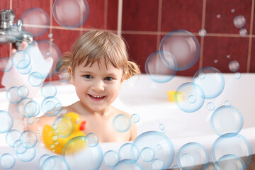 Cute little girl taking bath at home. Soap bubbles in air