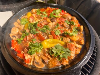 Beef meat and vegetables stew in black bowl with roasted baby potatoes. Dark background grill kamado.