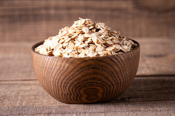 Raw oats in a wooden bowl on a wooden background. Organic food concept. 