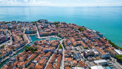 Aerial view of Grado, a picturesque seaside town in Friuli Venezia Giulia, Italy. The photo shows the historic old town with red-tiled roofs, charming harbor, long sandy beaches, blue water