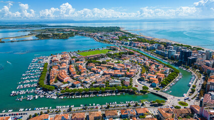 Aerial view of Grado, a picturesque seaside town in Friuli Venezia Giulia, Italy. The photo shows the historic old town with red-tiled roofs, charming harbor, long sandy beaches, blue water