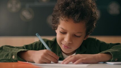 Closeup African American ethnic little school kid boy child concentrated writing notes test exam exercise in class lesson primary education learning knowledge write in copybook schoolboy pupil student - Powered by Adobe