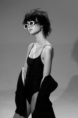 Black and white portrait of a stylish woman wearing sunglasses and a black dress with jacket,...