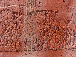 Closeup of a red stucco wall with a rough textured surface, visible pores and scratches