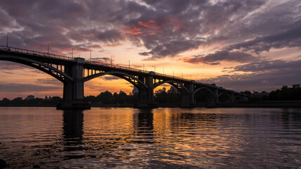 Fototapeta premium A bridge’s arches stand dark against the colorful sk