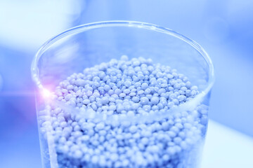 Close-up of small gray plastic pellets in a transparent glass container on a blurred background. Polymer materials for plastic injection molding
