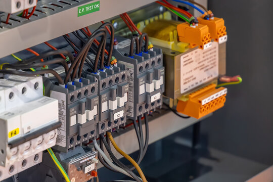 Close-up of an industrial electrical control panel featuring circuit breakers, relays, and wiring connections in a metallic enclosure. Electrical engineering concept