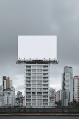 Obraz premium Large blank white billboard for advertisement on top of building. An urban city view with cloudy sky in background creating an imposing modern cityscape