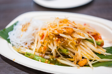 Traditional Thai cuisine spicy green papaya salad served on paper dish