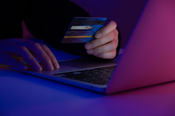 Hacker holding a credit card while accessing a system with a laptop. Concept of cybercrime, online fraud, identity theft, hacking, and digital security risk