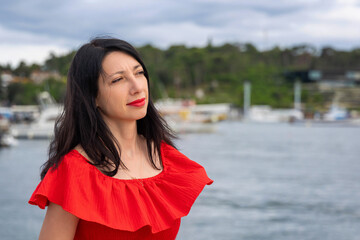 Thoughtful woman in red dress near water. A woman in a red dress gazes thoughtfully into the...