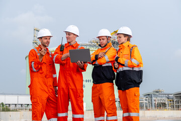 Workers in orange coveralls collaborate at a construction site while using technology for project...