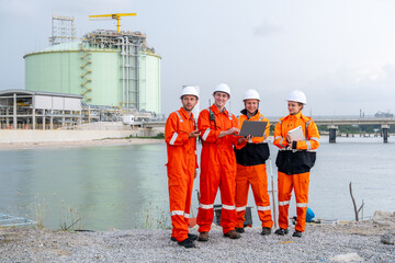 Group of workers in orange uniforms discussing project plans near industrial facility by the water
