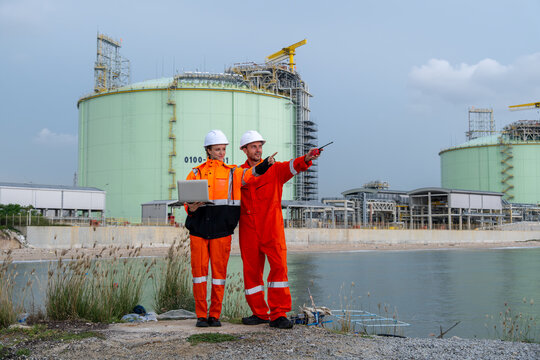 Workers in safety gear inspect industrial site near water during daytime