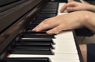 Fototapeta premium Close-up view of hands playing piano keys, showcasing the elegant black and white keys, highlighting musical expression and the art of performance in a cozy environment