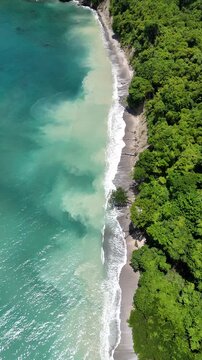 Aerial view of turquoise waves crash into sandy shores in Cabo Blanco Reserve, Costa Rica
