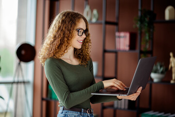 Charming young woman working on a laptop in a modern interior, showcasing casual style and creativity