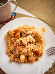 Delicious pilaf with chicken and carrots served on white plate with fork and tea