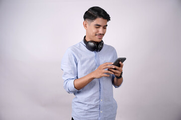 A young Asian man using his smartphone to chat or surf the internet and use social networks wearing...