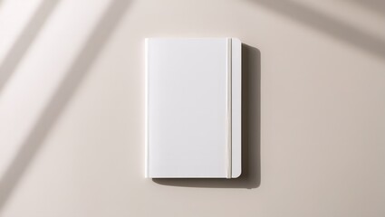 Minimalist flat lay of a blank white hardcover notebook on a neutral surface with elegant shadow play. Concept for branding, notes, or personal planning