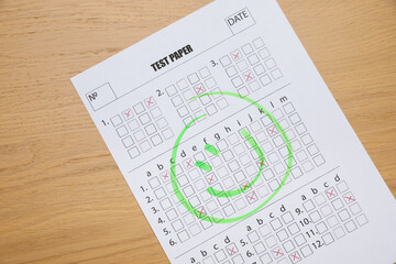 Answer sheet with drawn happy face on wooden table, top view. Student passing exam