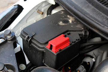 Close-up of car battery compartment with black plastic housing and red terminal cover. Located in...