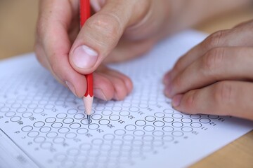 Student filling out multiple choice test at table, closeup. Passing exam